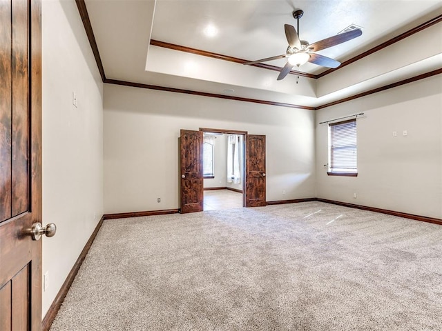 carpeted spare room with a raised ceiling, crown molding, and baseboards