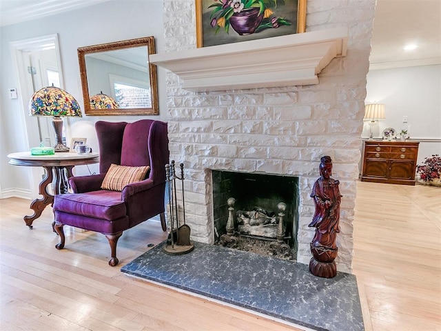 living area featuring a fireplace with raised hearth, baseboards, ornamental molding, and wood finished floors