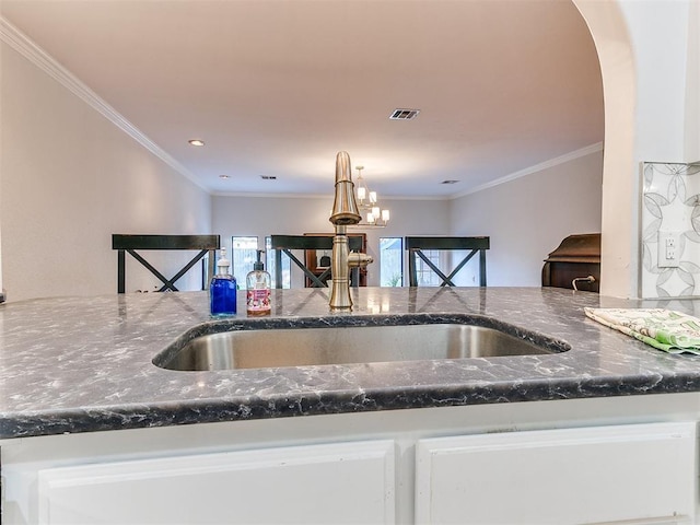 kitchen with dark stone counters, arched walkways, a sink, white cabinetry, and crown molding