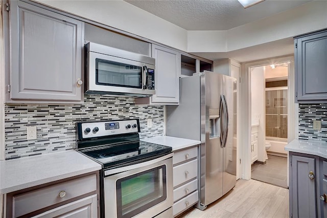 kitchen featuring gray cabinets, light hardwood / wood-style floors, backsplash, and appliances with stainless steel finishes