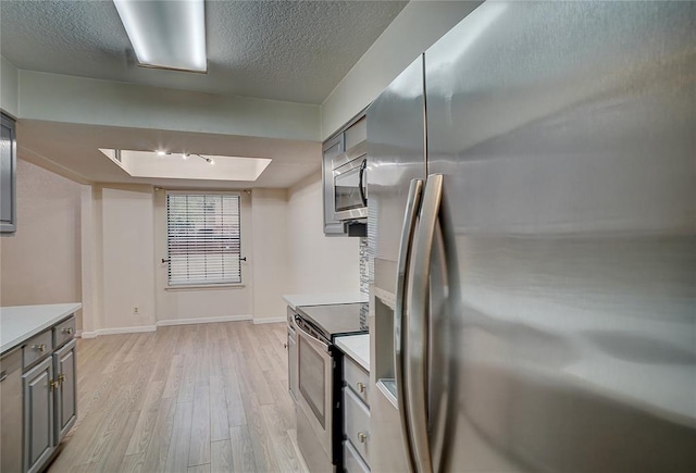 kitchen with appliances with stainless steel finishes, a textured ceiling, light hardwood / wood-style flooring, and gray cabinetry