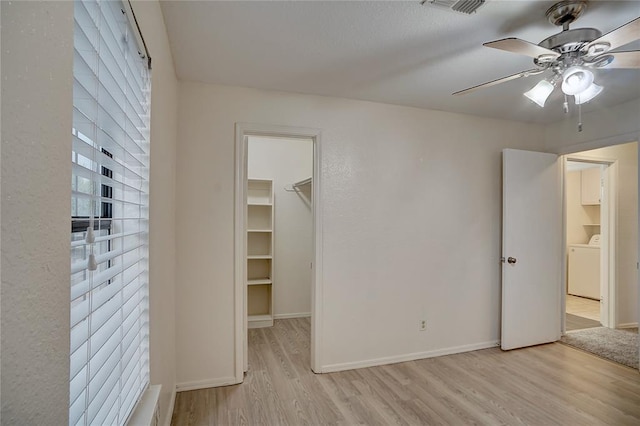 unfurnished bedroom featuring a spacious closet, ceiling fan, light hardwood / wood-style flooring, washer / clothes dryer, and a closet