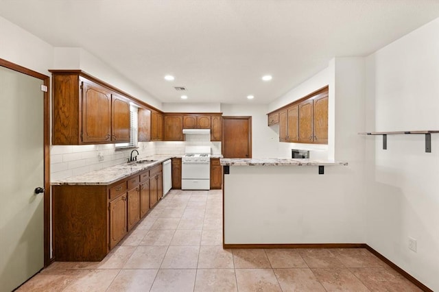 kitchen featuring light stone countertops, sink, kitchen peninsula, white appliances, and decorative backsplash