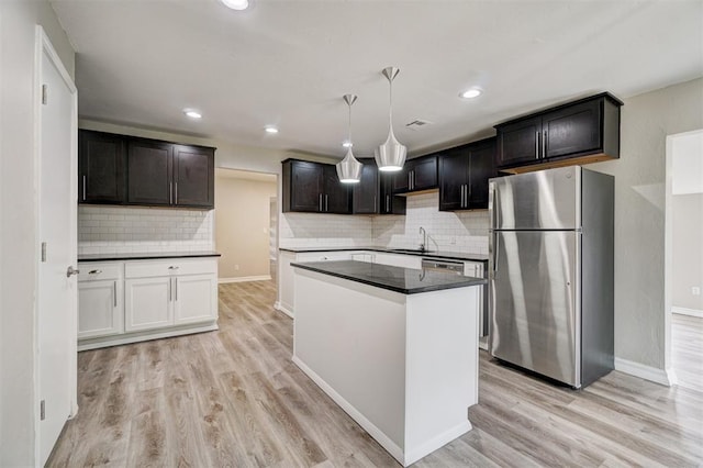 kitchen with sink, light wood-type flooring, appliances with stainless steel finishes, tasteful backsplash, and decorative light fixtures