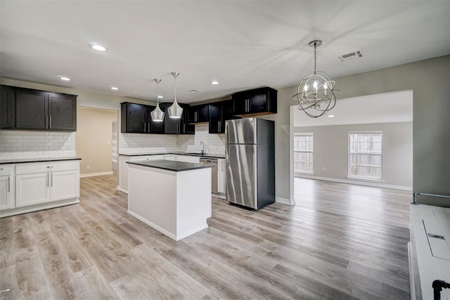 kitchen featuring hanging light fixtures, stainless steel appliances, backsplash, a chandelier, and light wood-type flooring