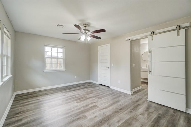 unfurnished bedroom featuring ceiling fan, a barn door, wood-type flooring, and a closet