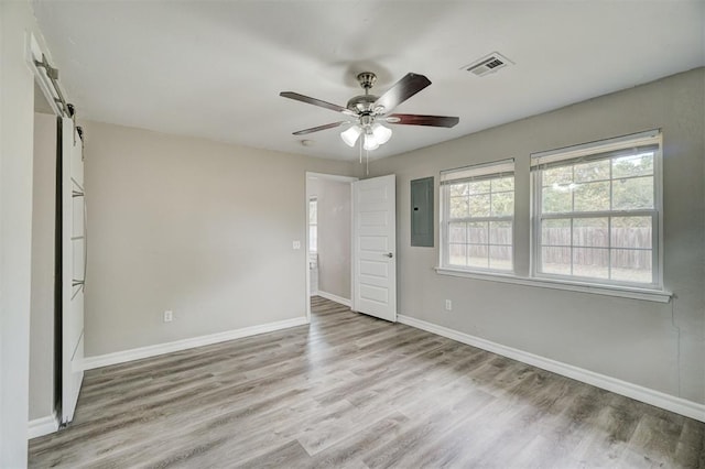 unfurnished bedroom featuring ceiling fan, a barn door, light wood-type flooring, and electric panel