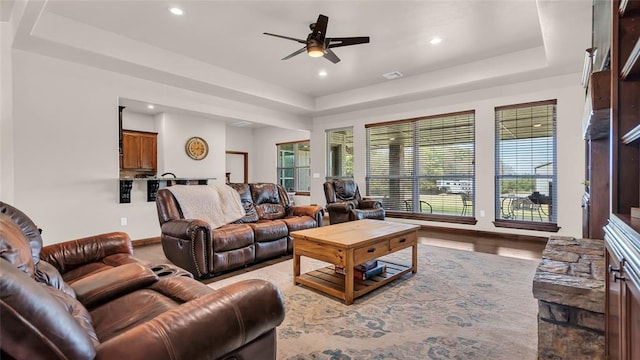 living room featuring ceiling fan, light wood-type flooring, and a tray ceiling