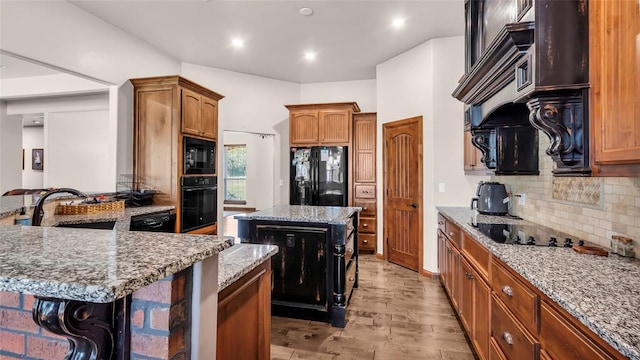 kitchen with black appliances, a kitchen island, light stone counters, and light wood-type flooring