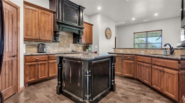 kitchen with a center island, dark wood-type flooring, sink, decorative backsplash, and light stone counters