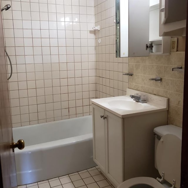 full bathroom with tile patterned floors, vanity, tiled shower / bath combo, tile walls, and toilet