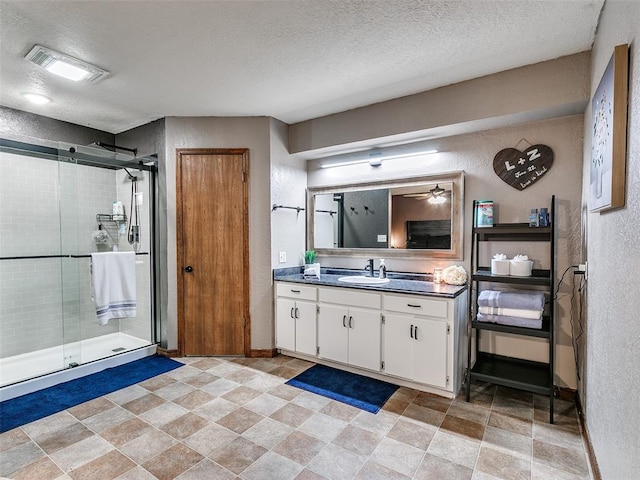 bathroom featuring vanity, ceiling fan, a shower with door, and a textured ceiling