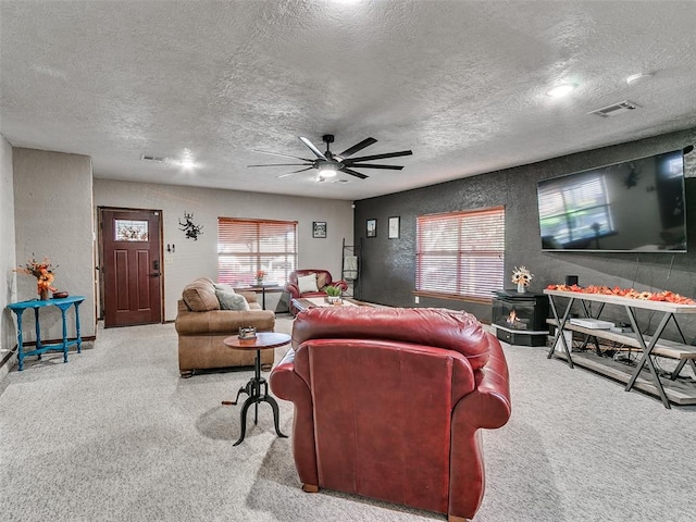 living room with carpet flooring, ceiling fan, a wood stove, and a textured ceiling