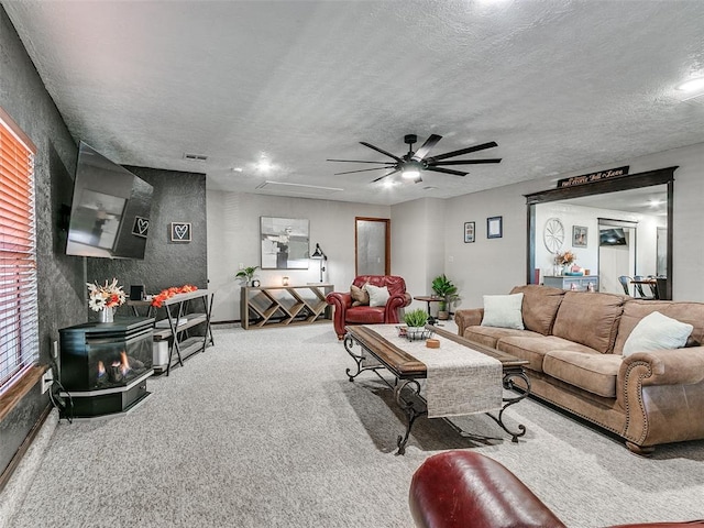 living room featuring a wood stove, ceiling fan, carpet floors, and a textured ceiling