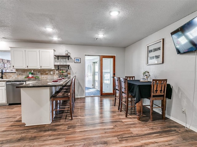 kitchen with a kitchen breakfast bar, stainless steel dishwasher, dark hardwood / wood-style floors, tasteful backsplash, and white cabinetry