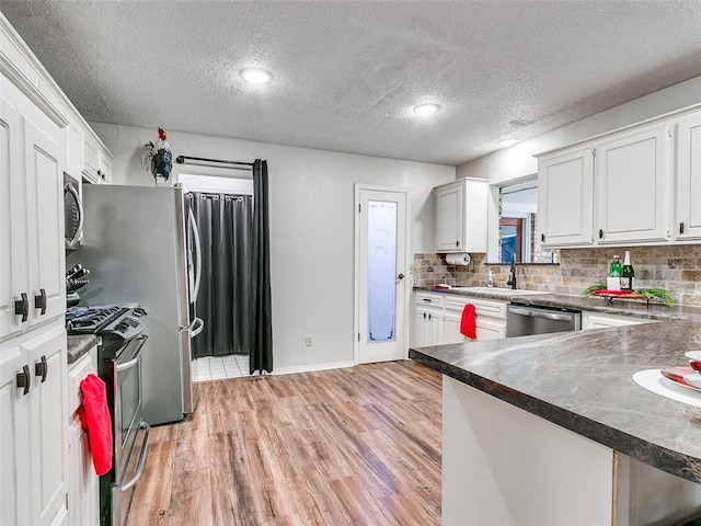 kitchen with light wood-type flooring, a textured ceiling, stainless steel appliances, sink, and white cabinets