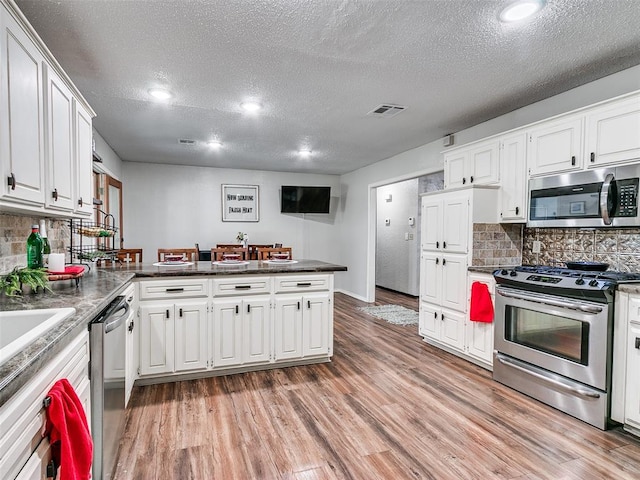 kitchen with white cabinets, decorative backsplash, kitchen peninsula, and stainless steel appliances