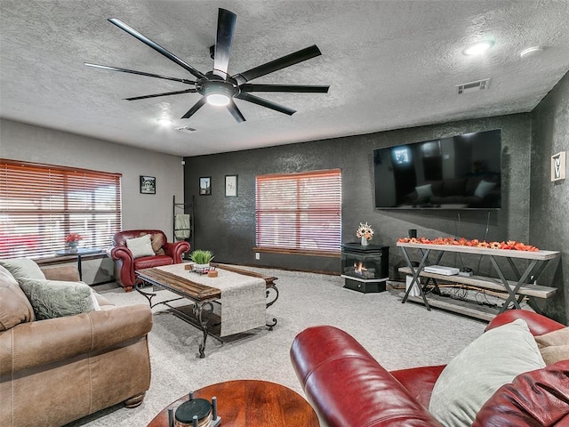 carpeted living room with a wood stove, ceiling fan, and a textured ceiling