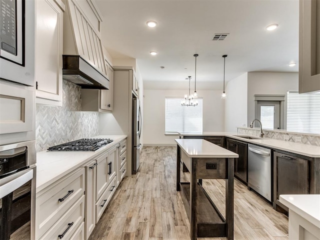 kitchen with stainless steel appliances, sink, decorative light fixtures, a chandelier, and light hardwood / wood-style floors