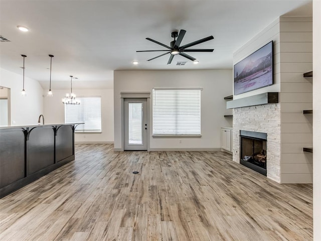 unfurnished living room featuring a fireplace, ceiling fan with notable chandelier, and light hardwood / wood-style floors