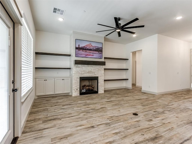 unfurnished living room featuring a stone fireplace, ceiling fan, and light hardwood / wood-style floors