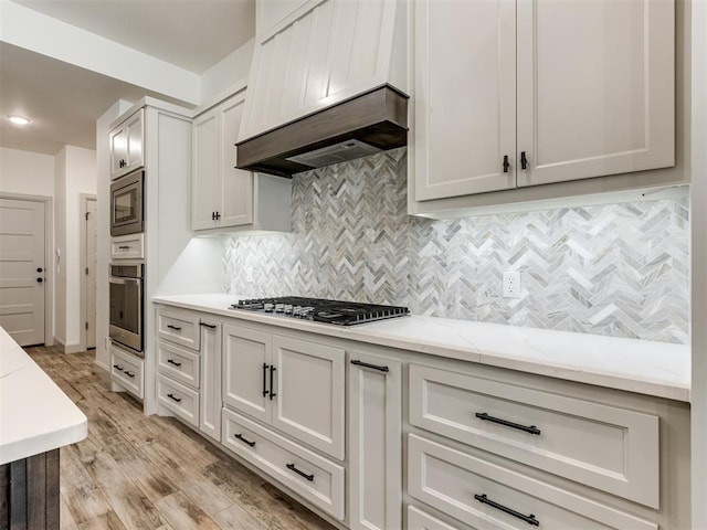 kitchen with light wood-type flooring, tasteful backsplash, light stone counters, custom exhaust hood, and stainless steel appliances