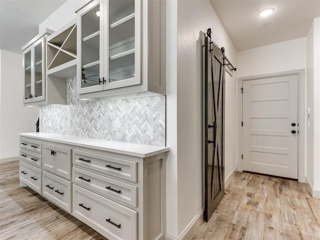 kitchen featuring white cabinets, a barn door, light hardwood / wood-style flooring, and backsplash