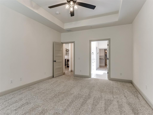 unfurnished bedroom with a tray ceiling, ceiling fan, light colored carpet, and a spacious closet