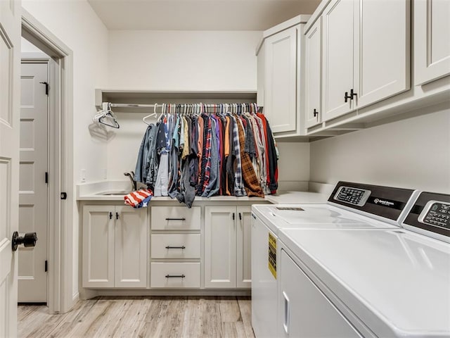 laundry area with washer and clothes dryer, cabinets, sink, and light hardwood / wood-style flooring