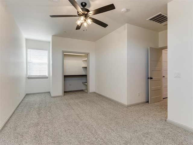 unfurnished bedroom featuring ceiling fan, light colored carpet, and a walk in closet