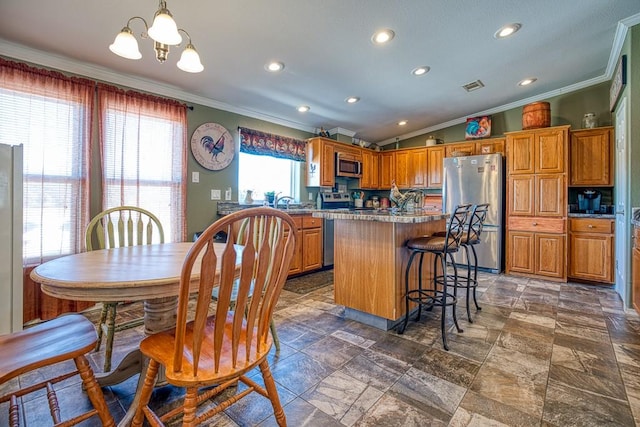 kitchen with appliances with stainless steel finishes, crown molding, a notable chandelier, a center island, and hanging light fixtures