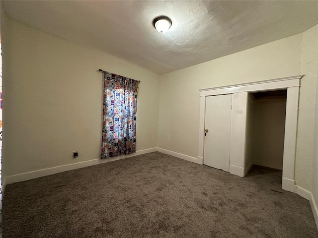 unfurnished bedroom with a textured ceiling, dark carpet, and a closet