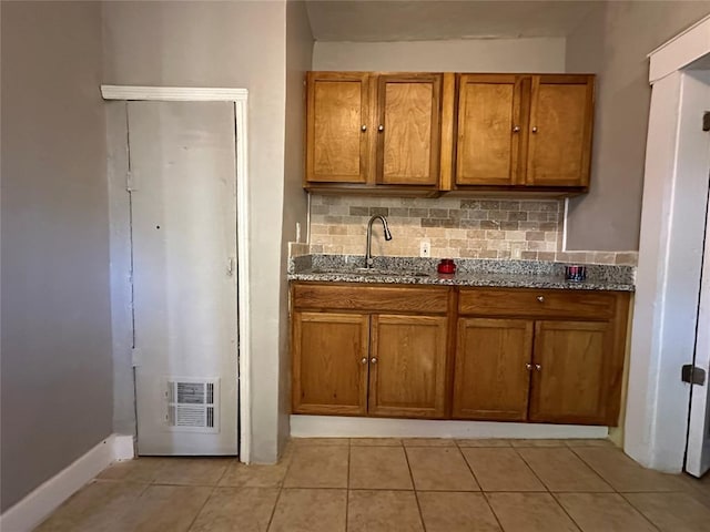 kitchen with tasteful backsplash, light stone countertops, sink, and light tile patterned floors