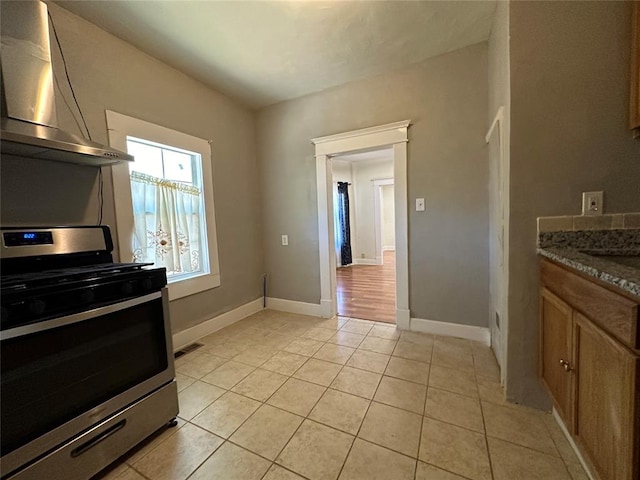 kitchen featuring gas stove, light tile patterned floors, dark stone counters, and range hood