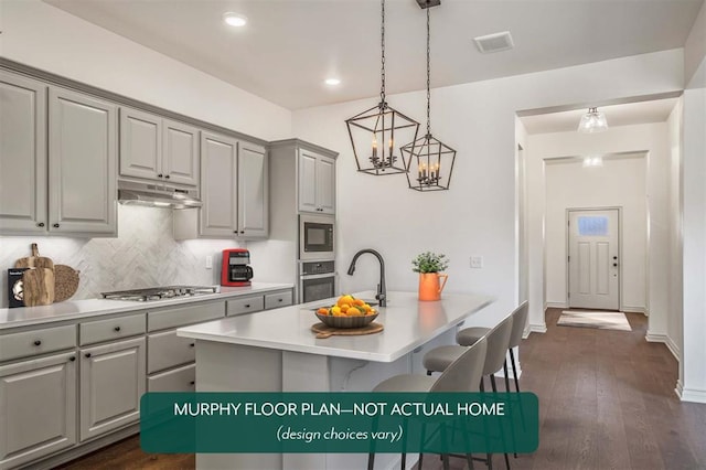 kitchen featuring gray cabinetry, dark wood-type flooring, pendant lighting, a center island with sink, and appliances with stainless steel finishes