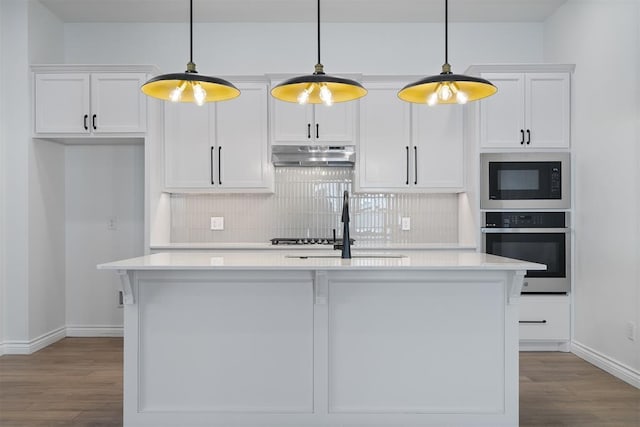 kitchen featuring decorative light fixtures, white cabinets, a kitchen island with sink, and oven