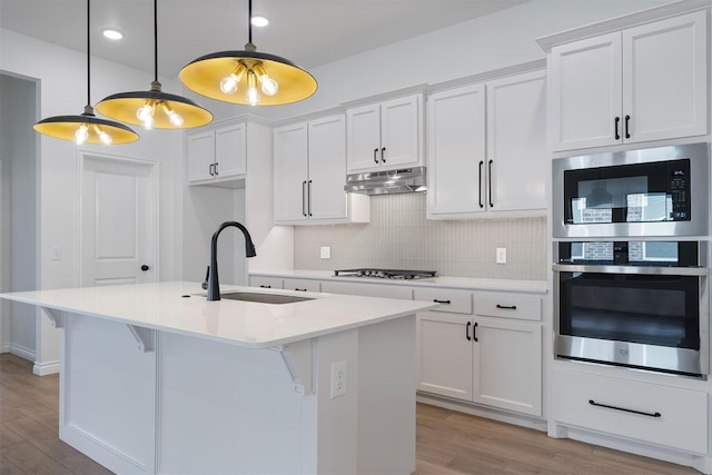 kitchen with sink, white cabinets, a kitchen island with sink, and decorative light fixtures