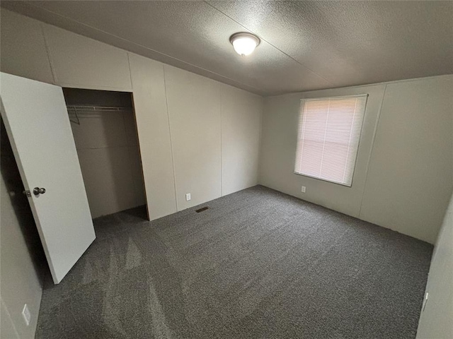 unfurnished bedroom featuring dark carpet, a textured ceiling, and a closet