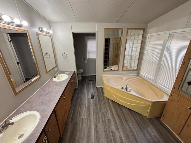 bathroom featuring a bath, hardwood / wood-style floors, a textured ceiling, toilet, and vanity