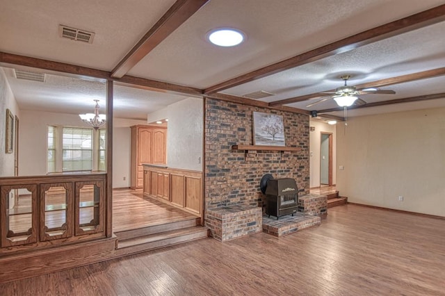 unfurnished living room with beam ceiling, a textured ceiling, light hardwood / wood-style floors, and a wood stove