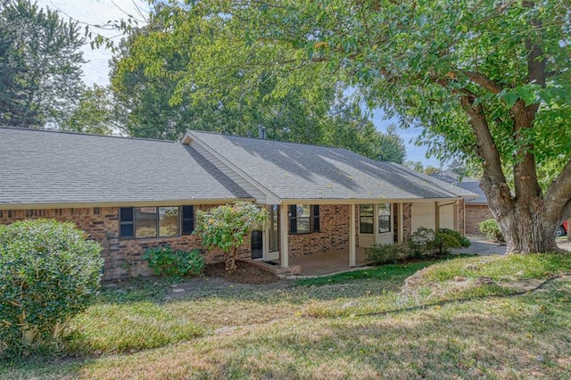 ranch-style home featuring an attached garage, brick siding, roof with shingles, and a front yard