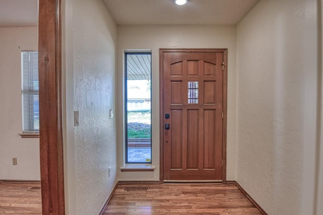 foyer entrance with a textured wall, baseboards, and wood finished floors