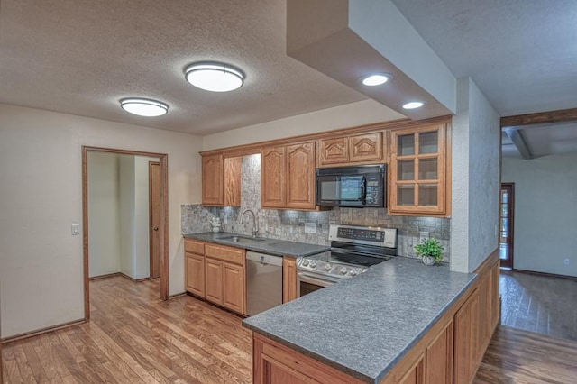 kitchen featuring stainless steel appliances, a sink, light wood-style floors, backsplash, and dark countertops