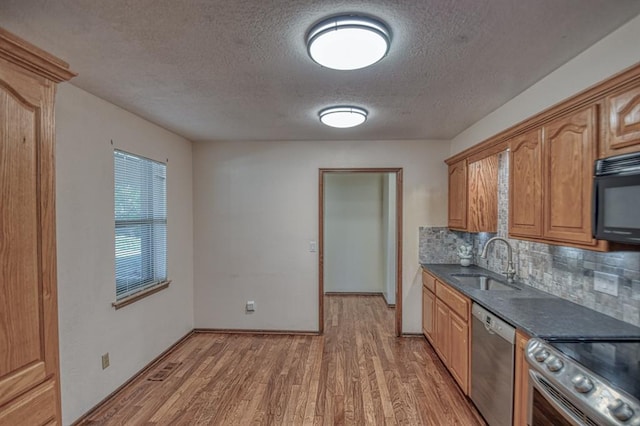 kitchen with stainless steel appliances, a sink, decorative backsplash, light wood finished floors, and dark countertops