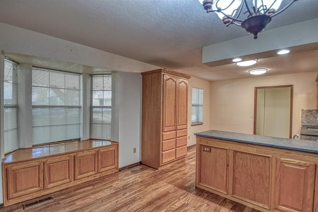 kitchen featuring visible vents, a textured ceiling, light wood-style flooring, and brown cabinets