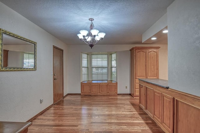 unfurnished dining area featuring baseboards, a textured wall, a textured ceiling, light wood-type flooring, and a chandelier