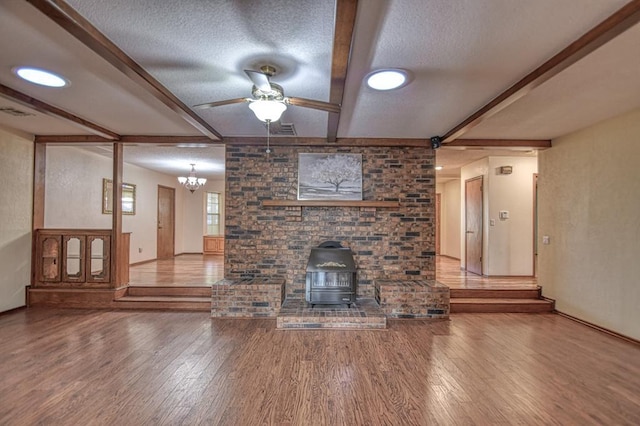 unfurnished living room with a wood stove, a textured ceiling, beamed ceiling, and wood finished floors