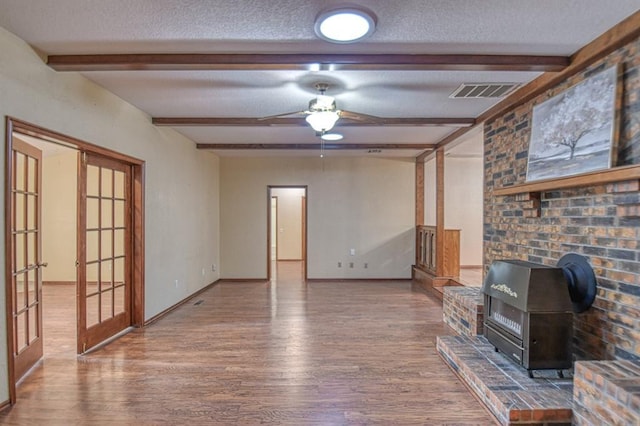 unfurnished living room with beam ceiling, visible vents, a textured ceiling, and wood finished floors