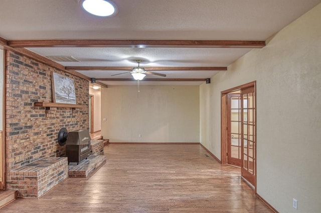 unfurnished living room with a textured ceiling, visible vents, wood finished floors, and beam ceiling