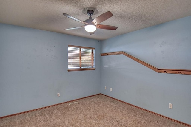 carpeted empty room featuring a textured ceiling, baseboards, visible vents, and a ceiling fan